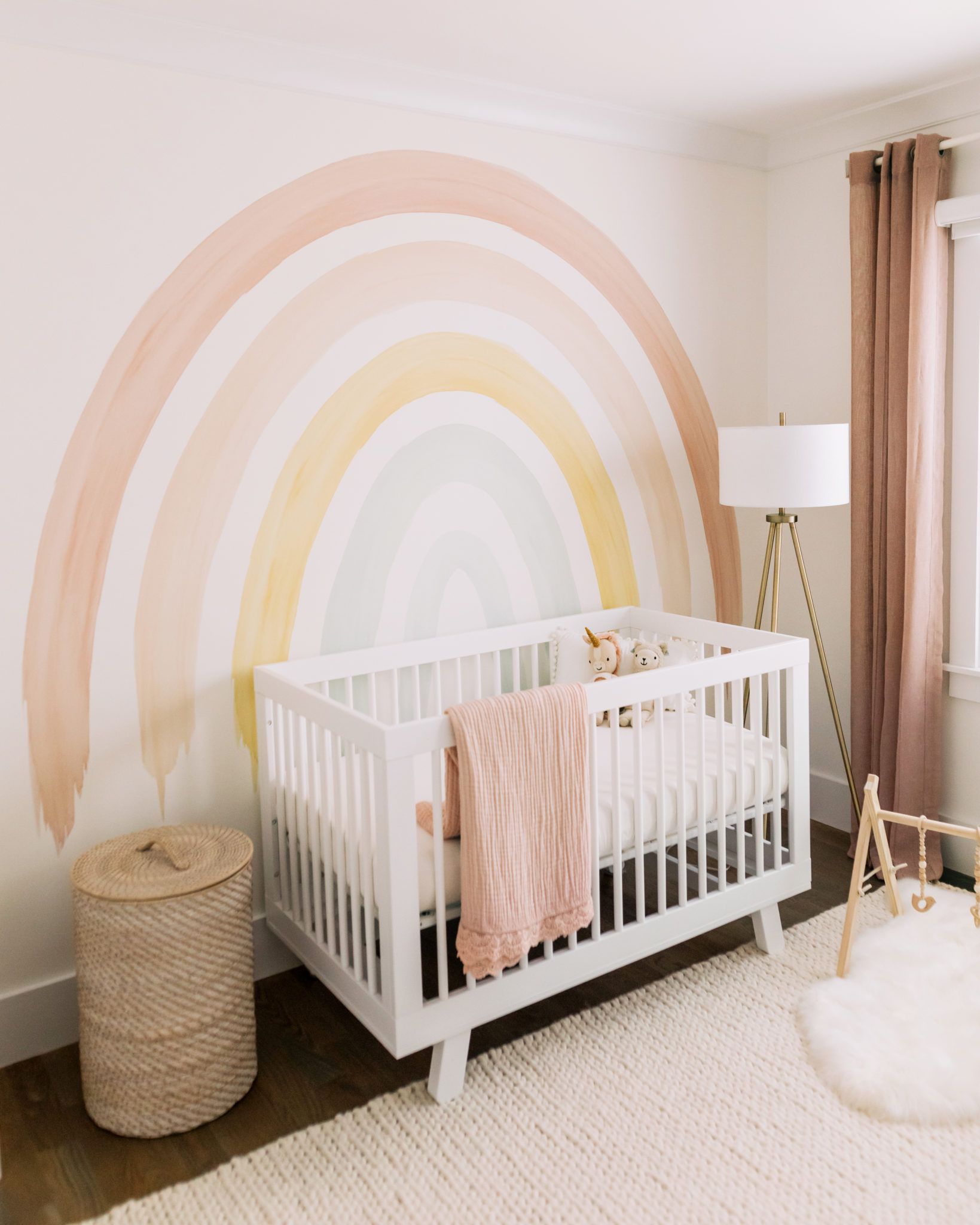 Bright and colorful watercolor rainbow nursery design featuring a white crib and light wood floors, illustrating effective nursery color psychology.