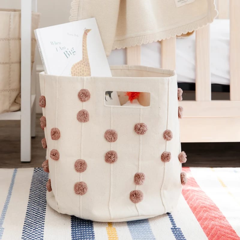 Cream nursery storage basket with pink pom-pom details.