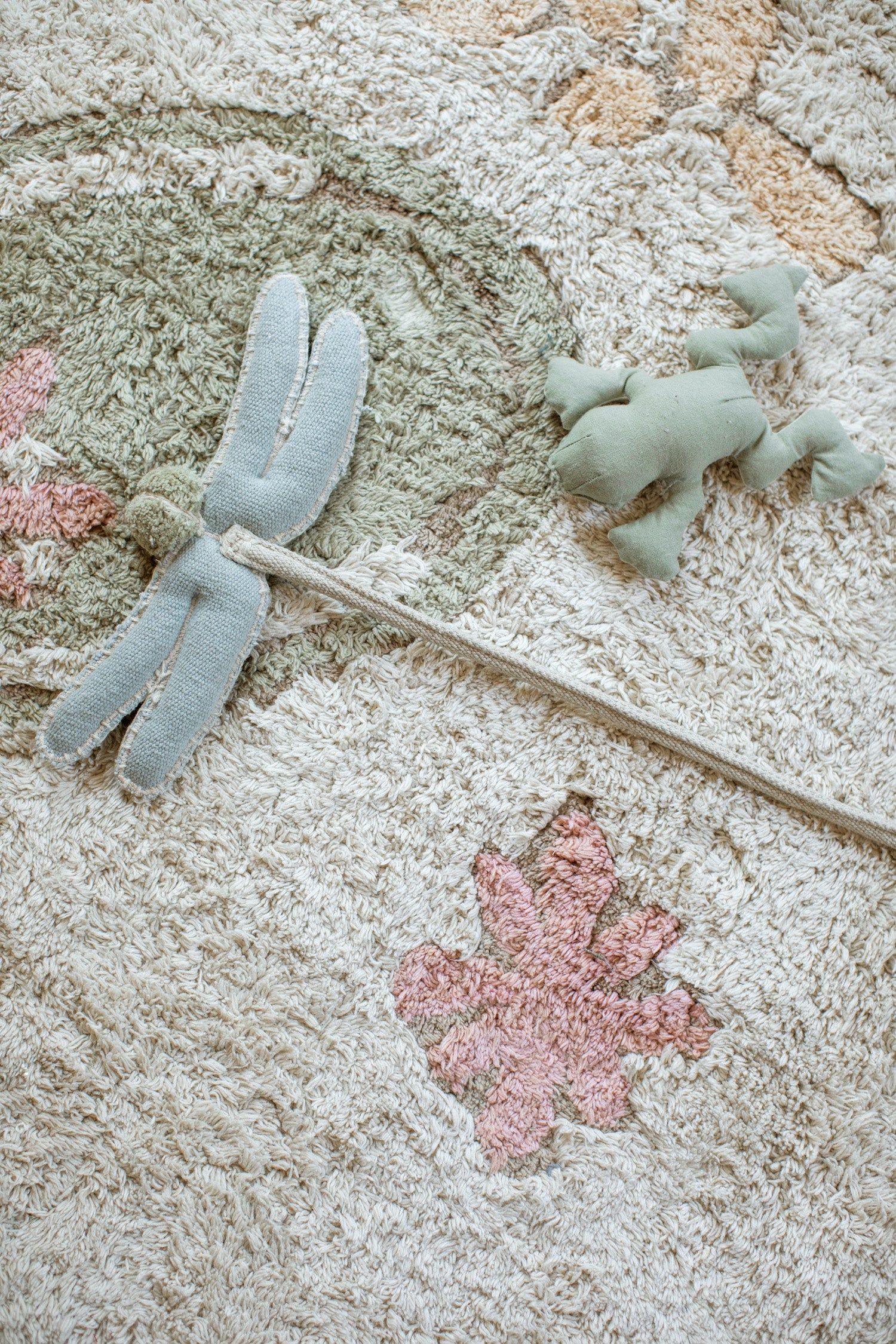 Close-up of a botanical kids’ rug with soft cream, sage green, and pink tones, featuring textured floral and leafy patterns.
