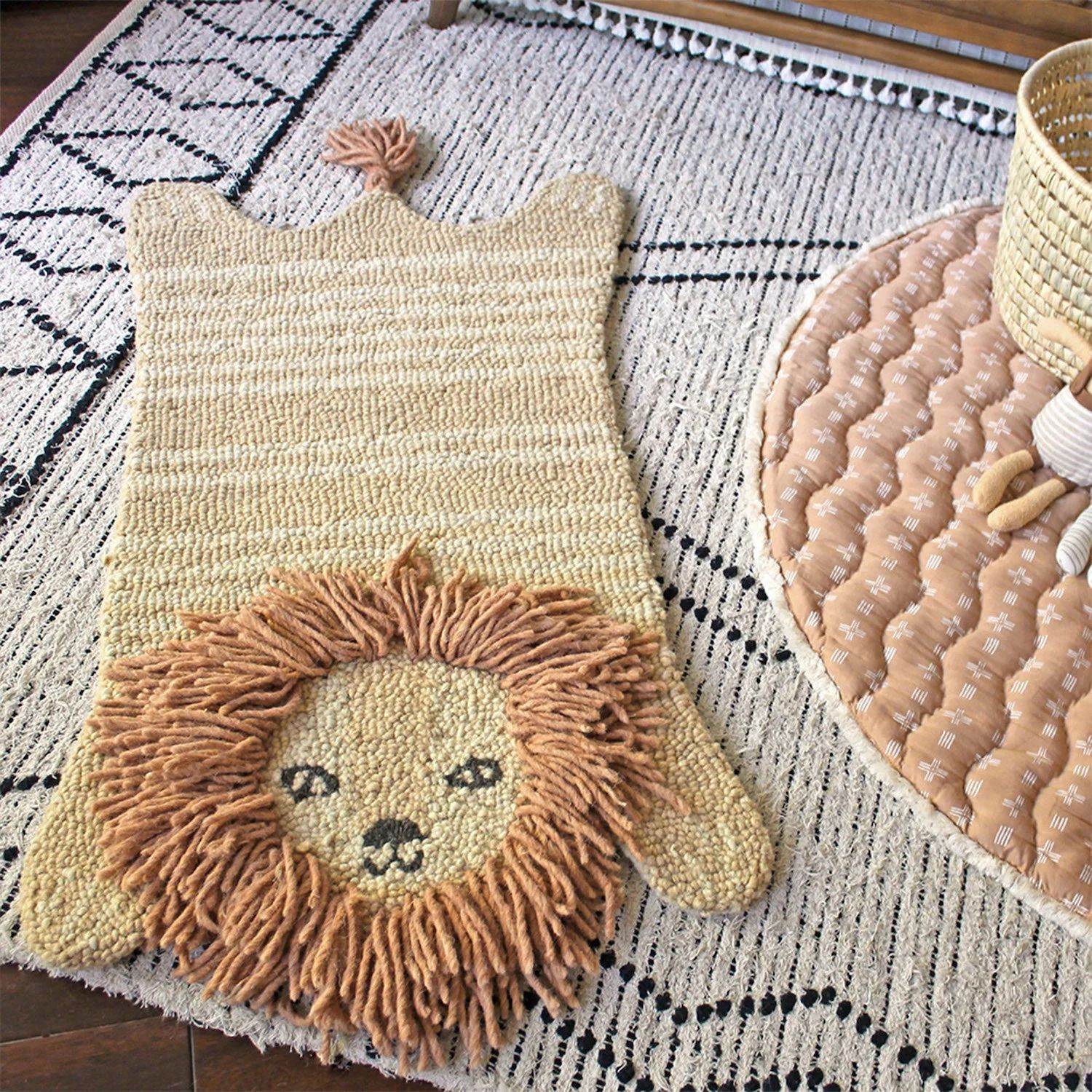 Lion-shaped kids’ rug with a textured mane and friendly face, placed over a black-and-white patterned rug in a cozy play area.
