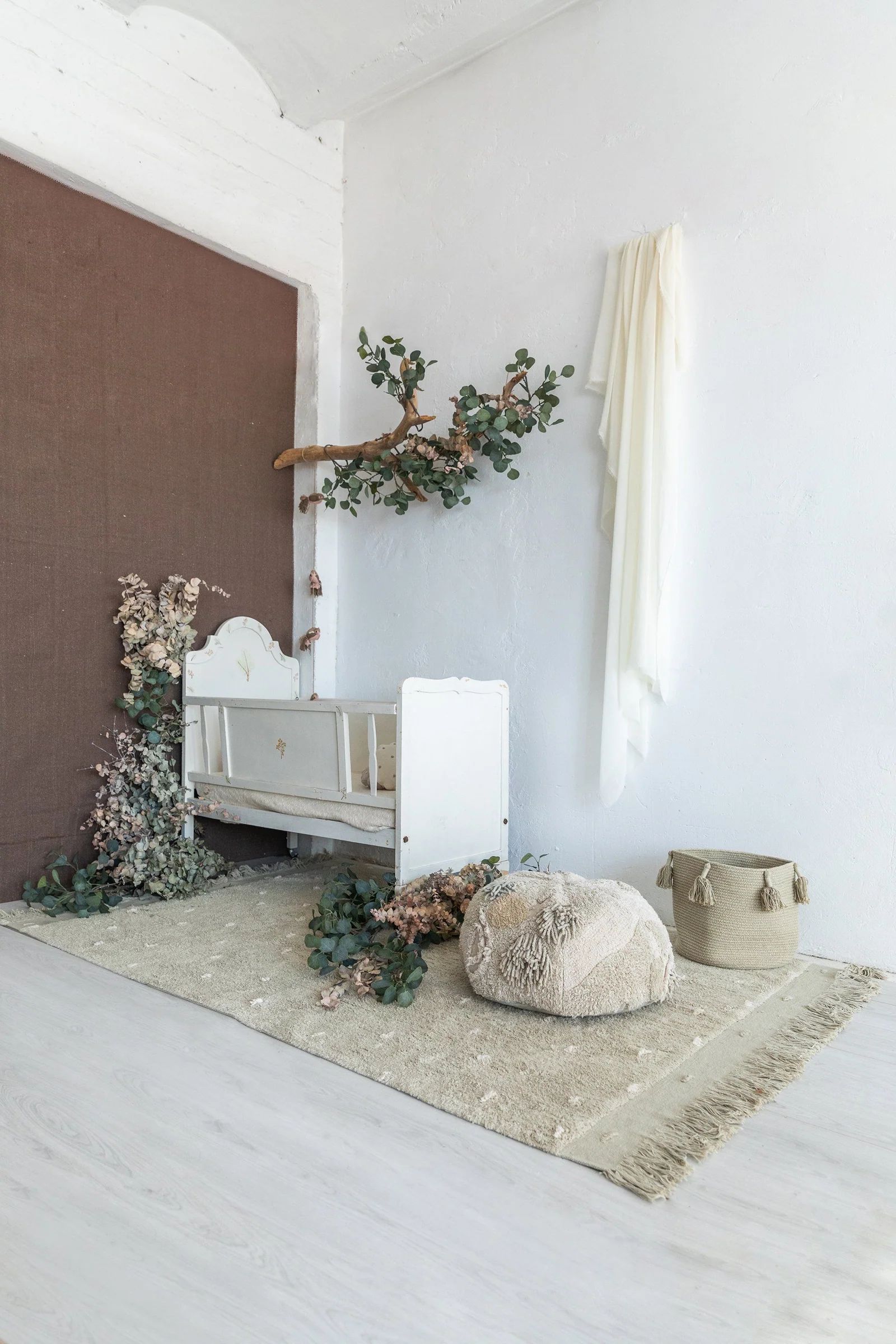 Neutral-toned kids’ nursery with a vintage-style wooden crib, eucalyptus decor, and a soft beige rug.